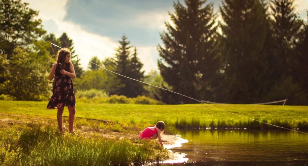 Two girls fishing in a stream on a sunny day.